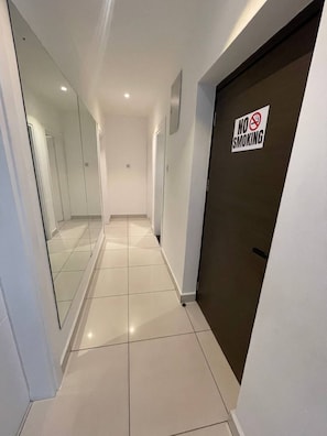 A corridor with a 'No Smoking' sign on a door, white tiled floors, and mirrored walls. - Luxury 3BR Apt w/ Pool, Gym Restaurant & DSTV - Embassy Gardens / 2 min from KIA (Accra)