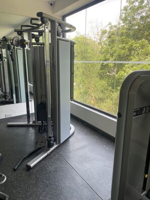 A gym with exercise equipment, a large window, and a view of greenery outside. - Luxury 3BR Apt w/ Pool, Gym Restaurant & DSTV - Embassy Gardens / 2 min from KIA (Accra)