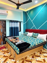 Quarto com colcha estampada, cabeceira estofada vermelha e piso com padrão geométrico.