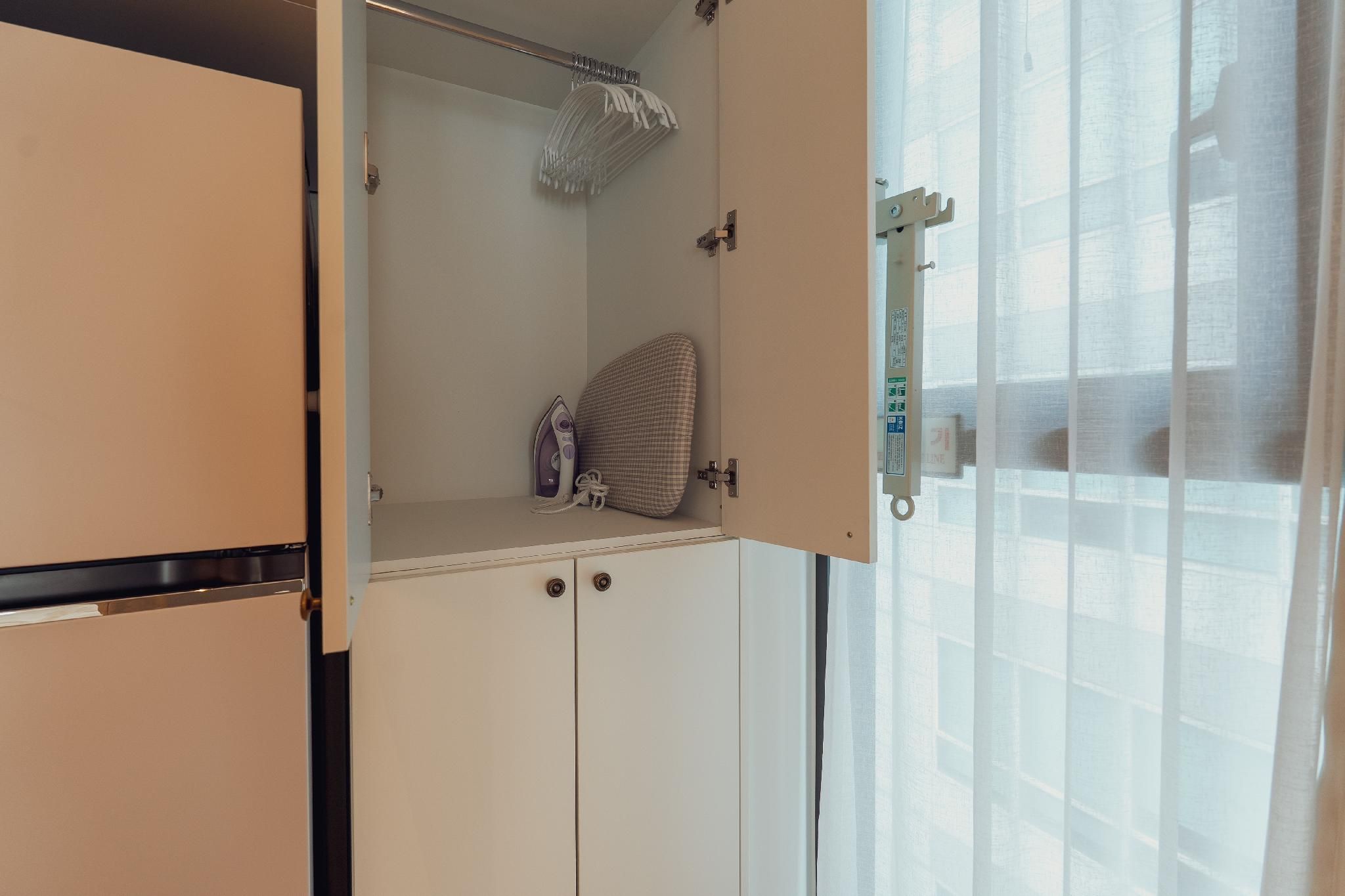 A room with a white wardrobe, a hanging rack, and a window with sheer curtains.