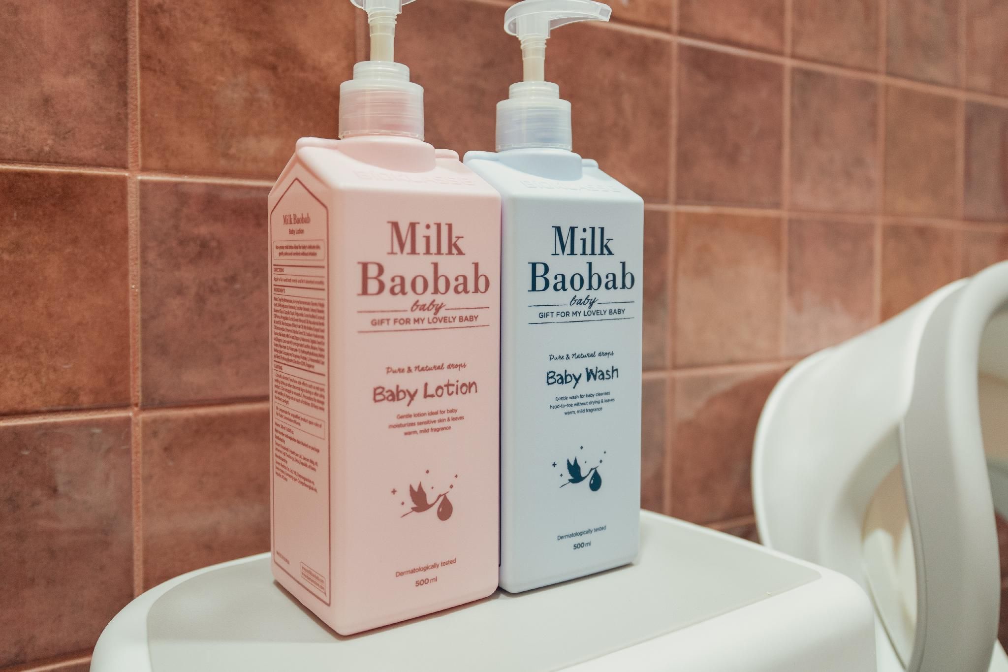 Dos productos para el cuidado del bebé, la loción Milk Baobab Baby y el jabón Baby Wash, sobre una superficie blanca frente a una pared de azulejos.