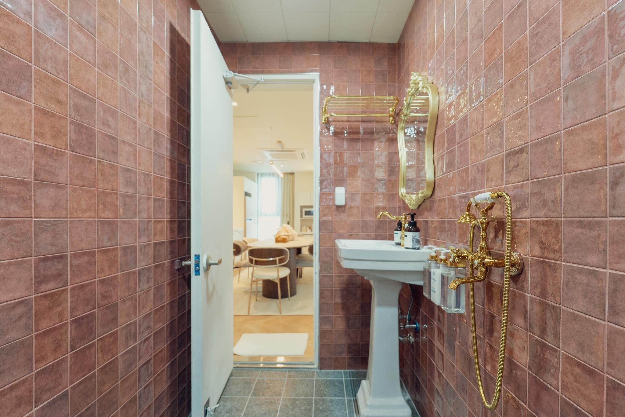 A bathroom with a white pedestal sink, gold fixtures, and a mirror with a gold frame.