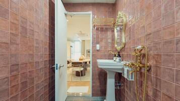 A bathroom with a white pedestal sink, gold fixtures, and a mirror with a gold frame.