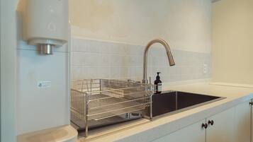 A kitchen with a stainless steel sink, a dish drying rack, and a soap dispenser.
