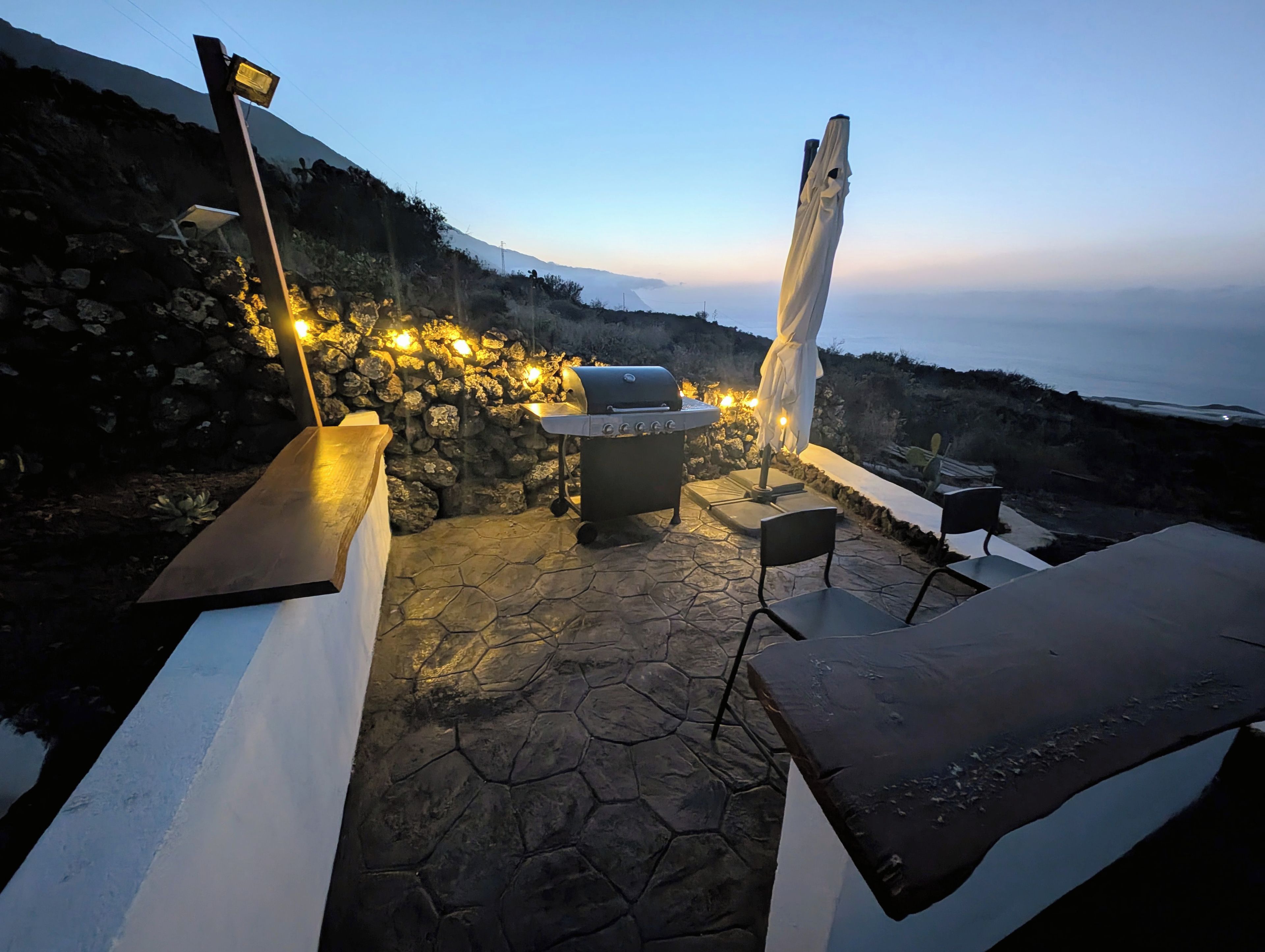 Une terrasse extérieure avec un sol en pierre, un barbecue et une vue sur l’océan.
