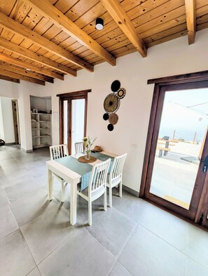 Un coin repas avec une table et des chaises, un élément décoratif fixé au mur, et une vue à travers une porte.