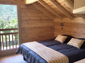 Een houten slaapkamer met een bed, kussens en uitzicht door een raam.