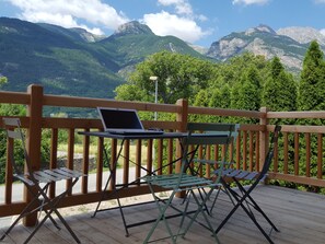 Eine Holzterrasse mit Tisch und Stühlen, mit Blick auf eine gebirgige Landschaft.