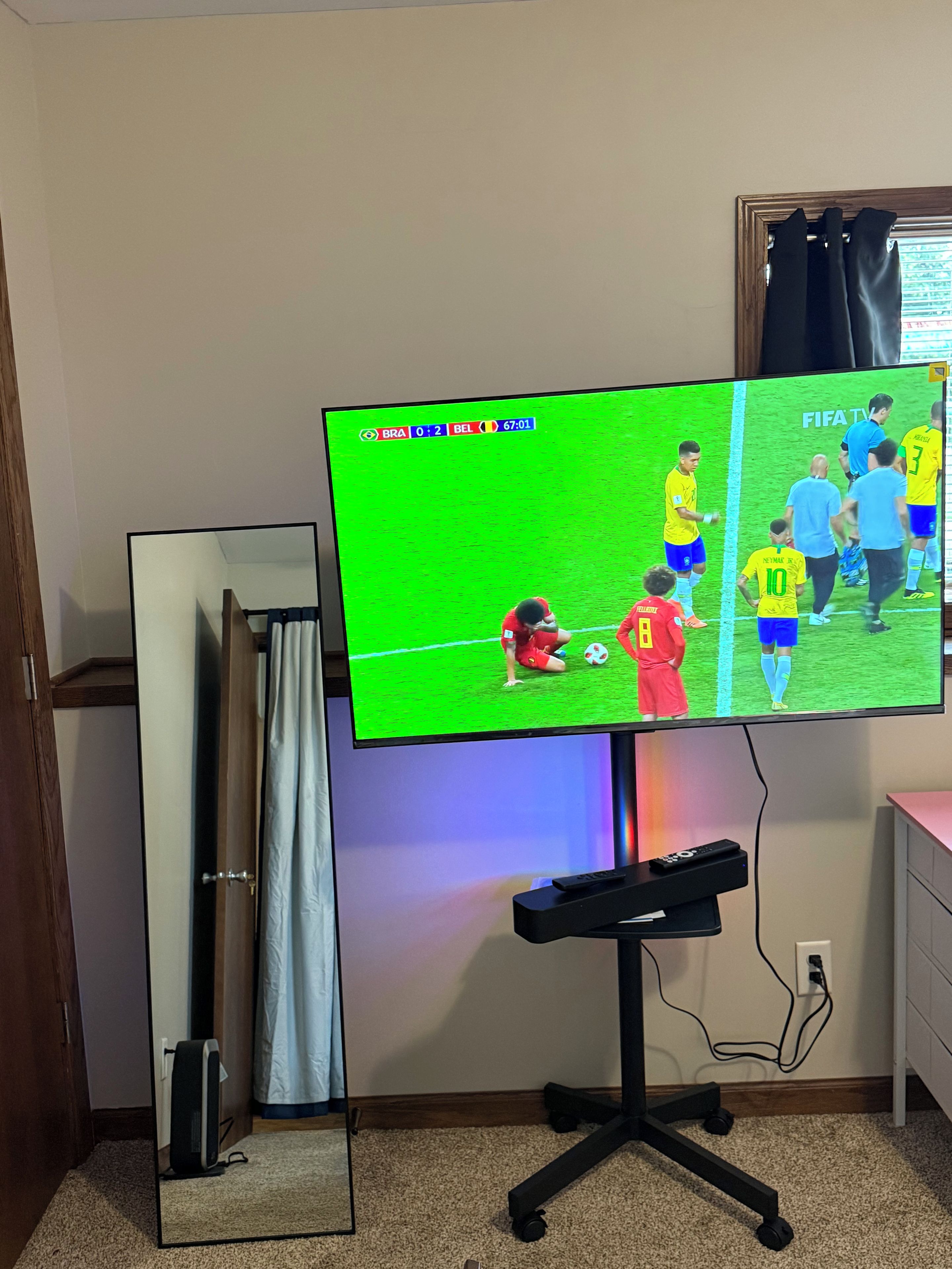 A television mounted on a stand with a remote control on a stand below it.