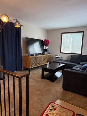 A living room with a flat-screen TV, a sofa, a coffee table, and a decorative lamp.