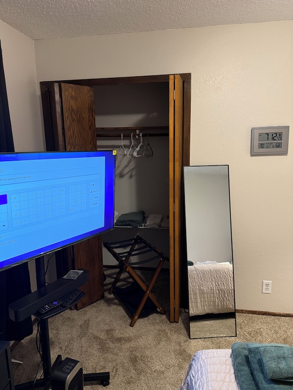 A room with a computer desk, a bed with a blue blanket, a mirror, and a wall clock.