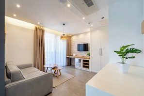 Een moderne woonkamer met een bank, een klein tafeltje, een aan een stenen muur bevestigde televisie, en een potplant.