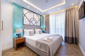 A modern hotel room with a large bed, a nightstand, a TV mounted on the wall, and a window with curtains. - Garni Casa Di Sofia (Rafajlovići)