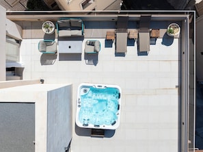 Una terraza con jacuzzi, mobiliario exterior y plantas en macetas.