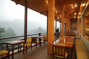 A wooden deck with tables and chairs, overlooking a forested area.
