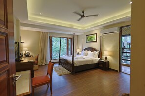 A spacious bedroom with a large bed, a ceiling fan, and a view of the outdoors through a sliding door. - Punarnava Wellness Resort & Spa (Dehradun)
