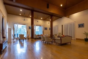 A spacious living area with a high ceiling, wooden beams, and a polished floor. There are multiple seating arrangements and a dining table.