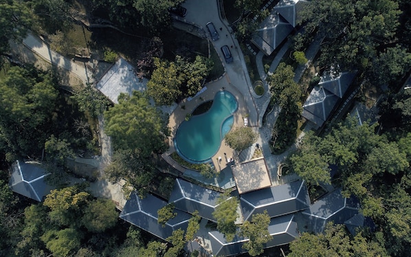 An aerial view of a residential area with a swimming pool surrounded by houses with unique roof designs.