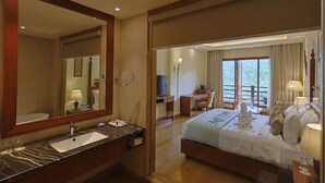 Une chambre d’hôtel avec un grand lit, un bureau, une salle de bain avec un lavabo et un miroir, et une vue sur l’extérieur.