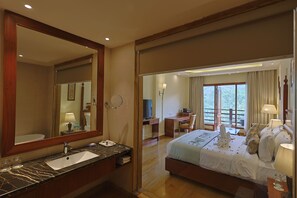 A hotel room with a large bed, a desk, a bathroom with a sink and mirror, and a view of the outdoors. - Punarnava Wellness Resort & Spa (Dehradun)