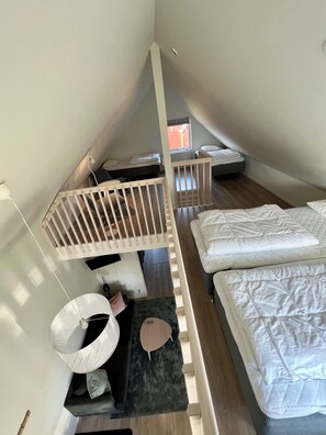 Ett rum med högt i tak och ett sluttande tak, en våningssäng, ett skrivbord och en stol.