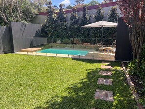 Ein Garten mit Schwimmbad, Glaszaun und einer Terrasse mit Gartenmöbeln.