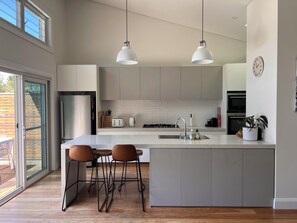 A modern kitchen with a large island, two pendant lights, and a view of the outdoors. - A refined family retreat with al fresco living, a pool and swift transport links (Banksia)