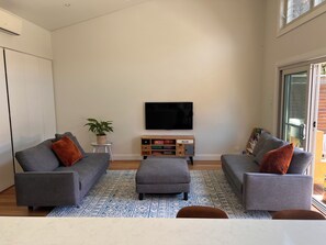 A modern living room with grey sofas, a coffee table, and a flat-screen TV mounted on the wall. - A refined family retreat with al fresco living, a pool and swift transport links (Banksia)