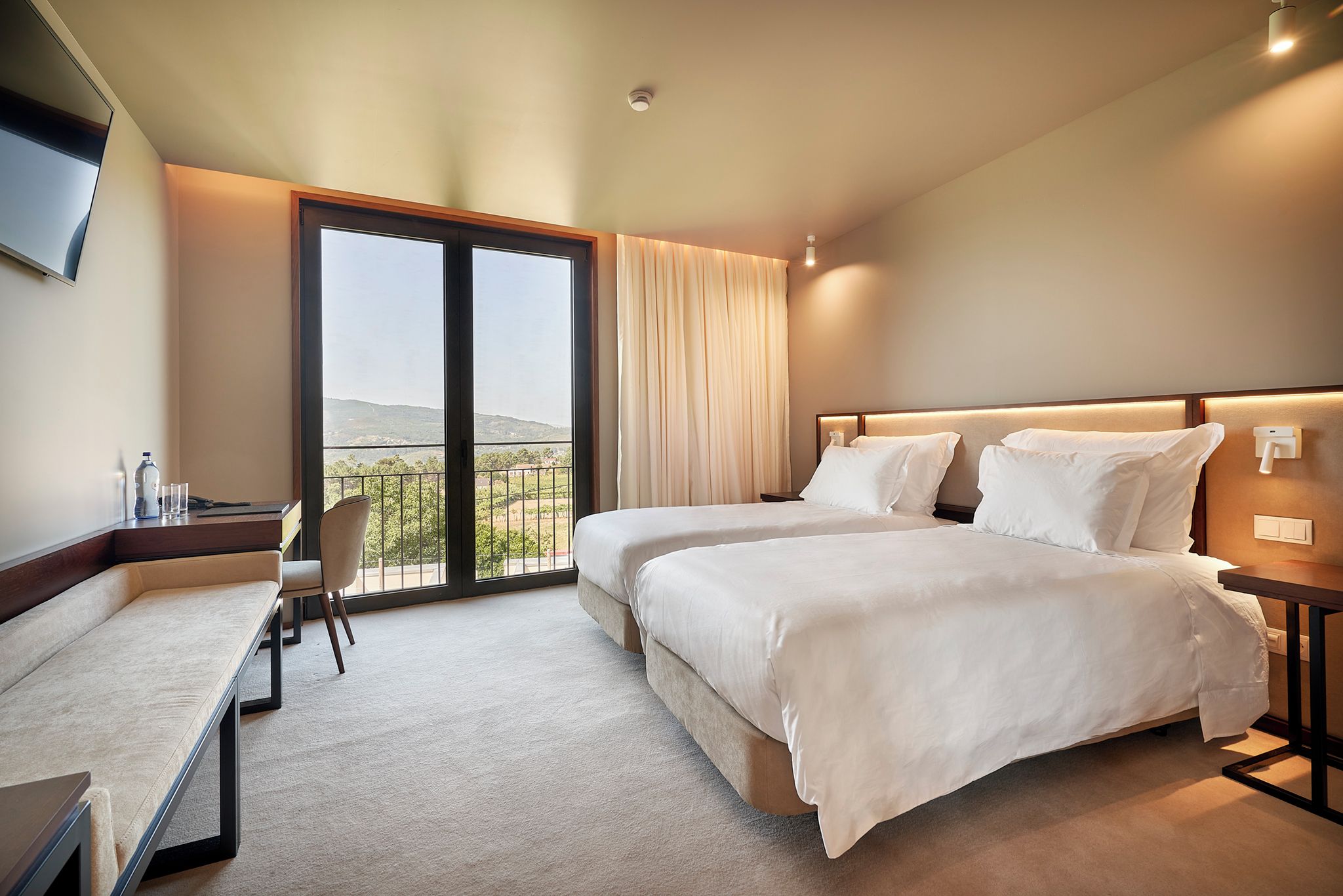 Een hotelkamer met twee bedden, een bureau, een stoel en een groot raam met uitzicht.