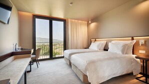A hotel room with two beds, a desk, a chair, and a large window with a view. - The Vinea Collection Hotel (Monção)