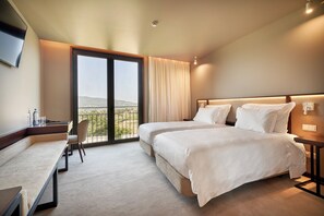 A hotel room with two beds, a desk, a chair, and a large window with a view. - The Vinea Collection Hotel (Monção)