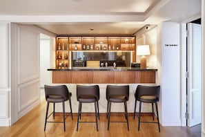 A bar area with a wooden counter, bar stools, and a variety of bottles.