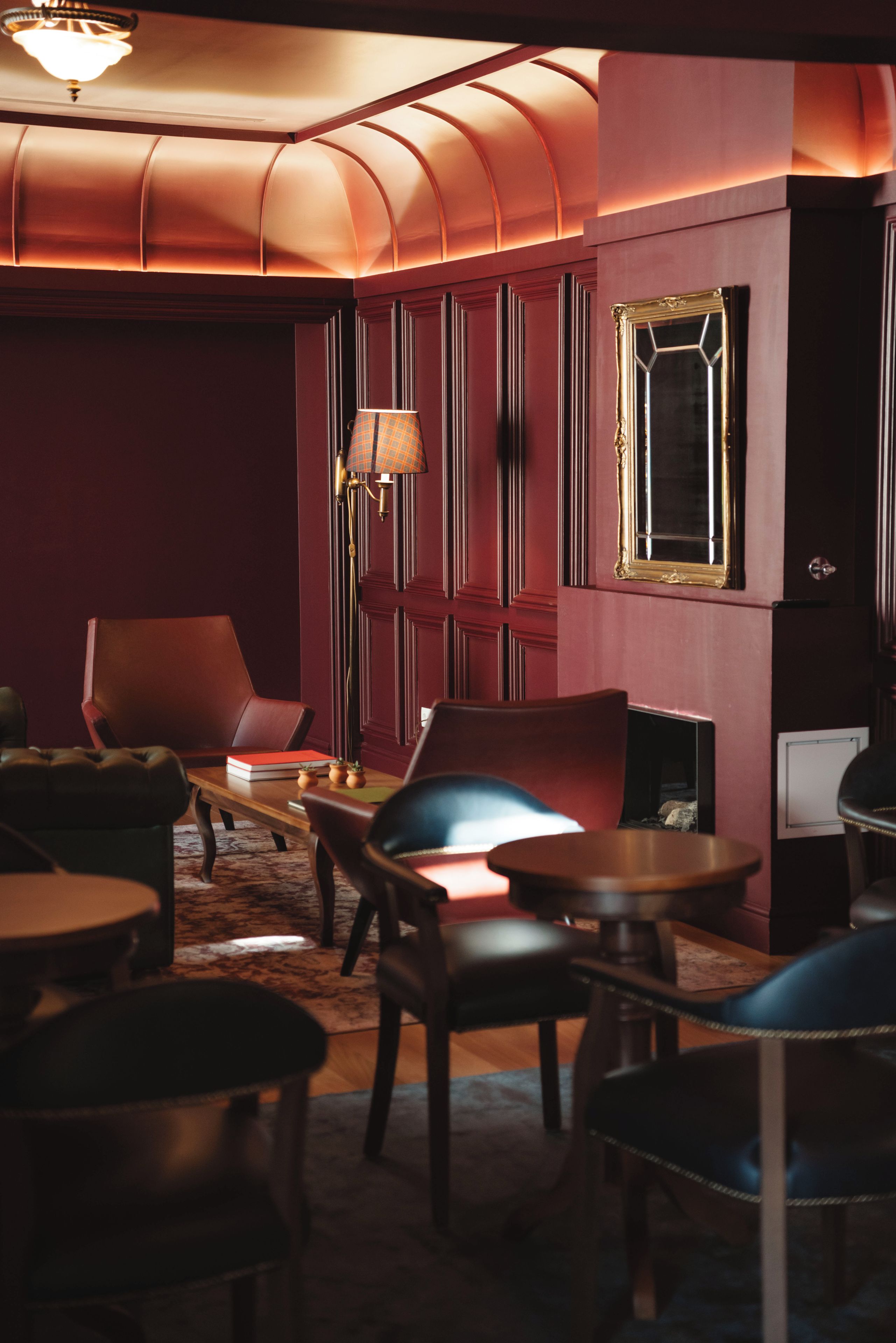 Une pièce faiblement éclairée, dotée d’un plafond voûté, d’un mur rouge et d’un plancher en bois. On y trouve plusieurs chaises et une table avec une lampe.