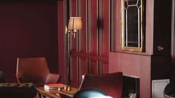 Una habitación tenuemente iluminada con techo curvo, pared roja y suelo de madera. Se observan varias sillas y una mesa con una lámpara.