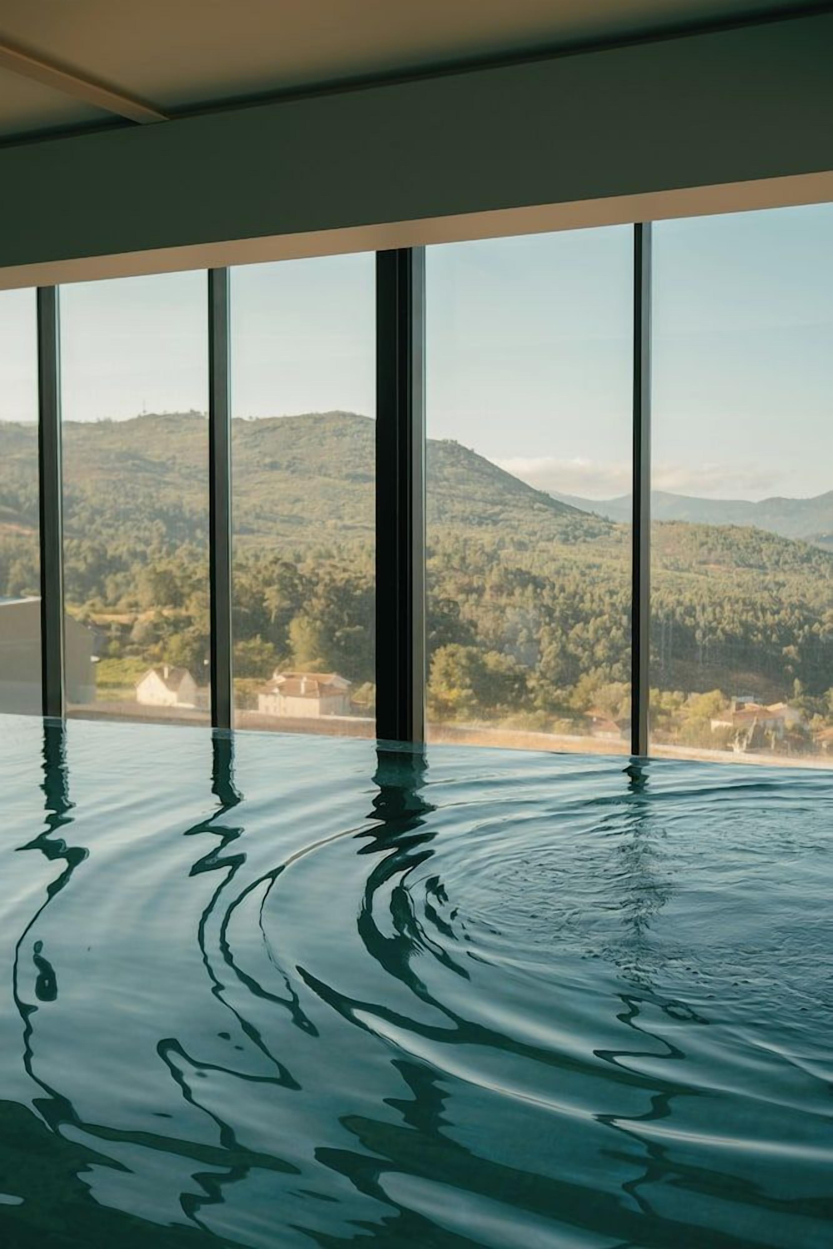 An indoor swimming pool with a view of a mountainous landscape through large windows.