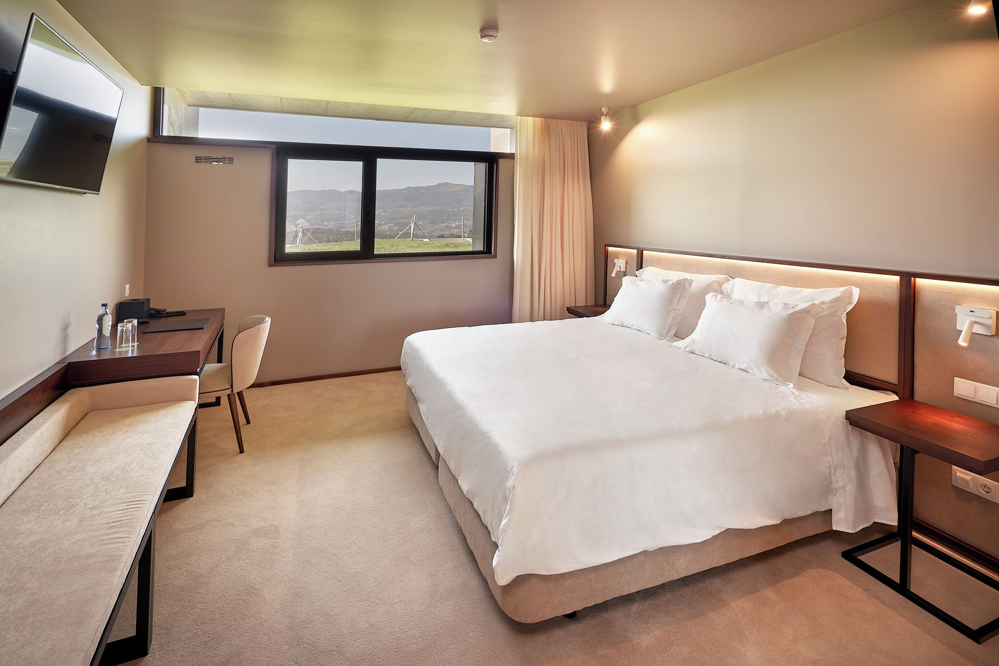 Une chambre d’hôtel dotée d’un grand lit, d’un bureau avec une chaise, d’un téléviseur à écran plat fixé au mur et d’une fenêtre donnant sur l’extérieur.