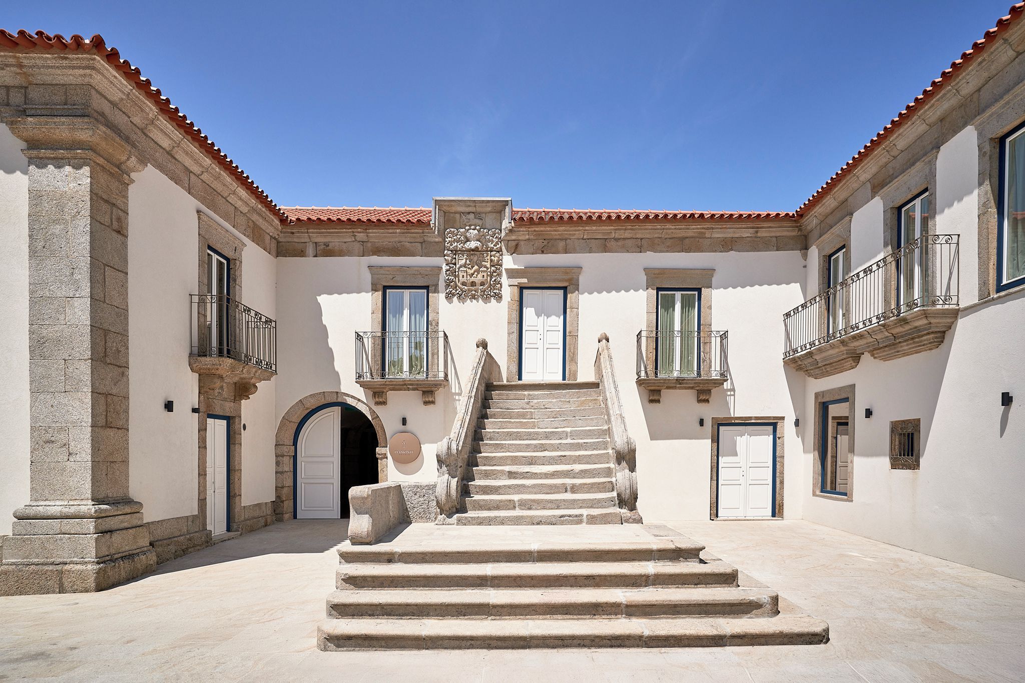 Un pati interior amb una escala central que condueix a una porta, flanquejat per edificis amb balcons i finestres.