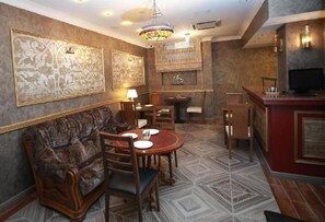 A dining area with a sofa, chairs, a table, and a bar area with a television. - West Inn Palace Hotel (Baku)