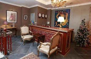 A lobby with a reception desk, two chairs, a Christmas tree, and a painting on the wall. - West Inn Palace Hotel (Baku)