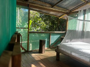 Una cama de madera con mosquitero, un banco de madera y vistas a la vegetación a través de una ventana con malla.