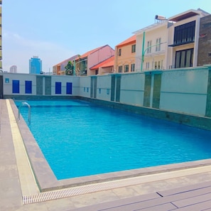 Una piscina con superficie de agua azul cristalina, rodeada por un muro bajo con barandilla metálica.