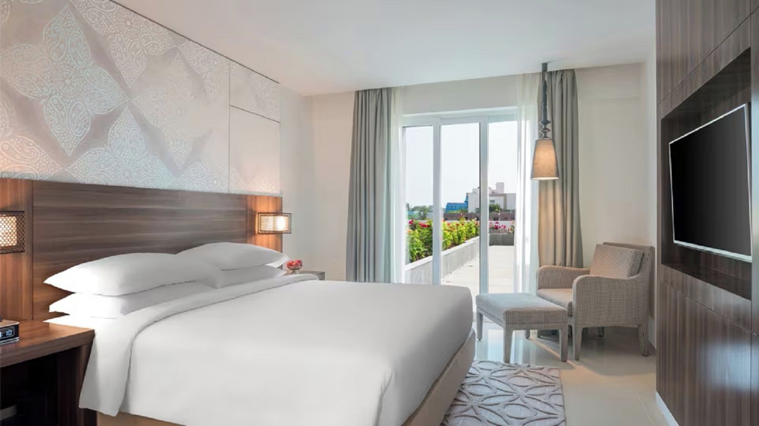 A hotel room with a large bed, a TV, a seating area, and a balcony with a view.
