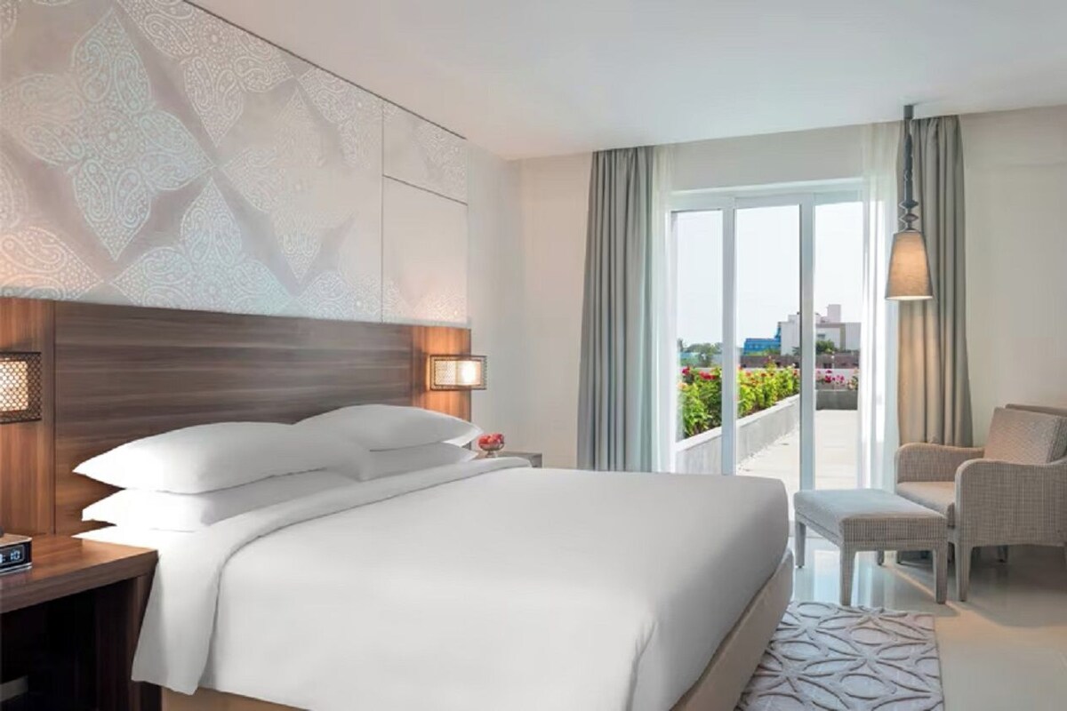 A hotel room with a large bed, a TV, a seating area, and a balcony with a view.