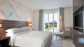 A hotel room with a large bed, a TV, a seating area, and a balcony with a view.