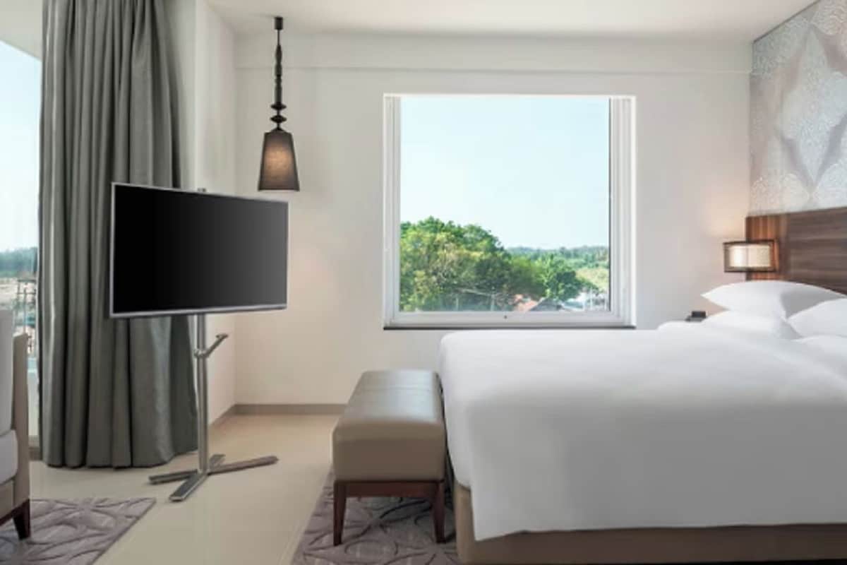 A hotel room with a bed, a TV, a window with a view, a bench, and a nightstand.