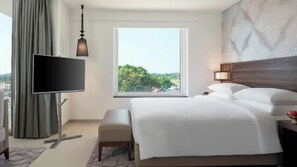 A hotel room with a bed, a TV, a window with a view, a bench, and a nightstand.