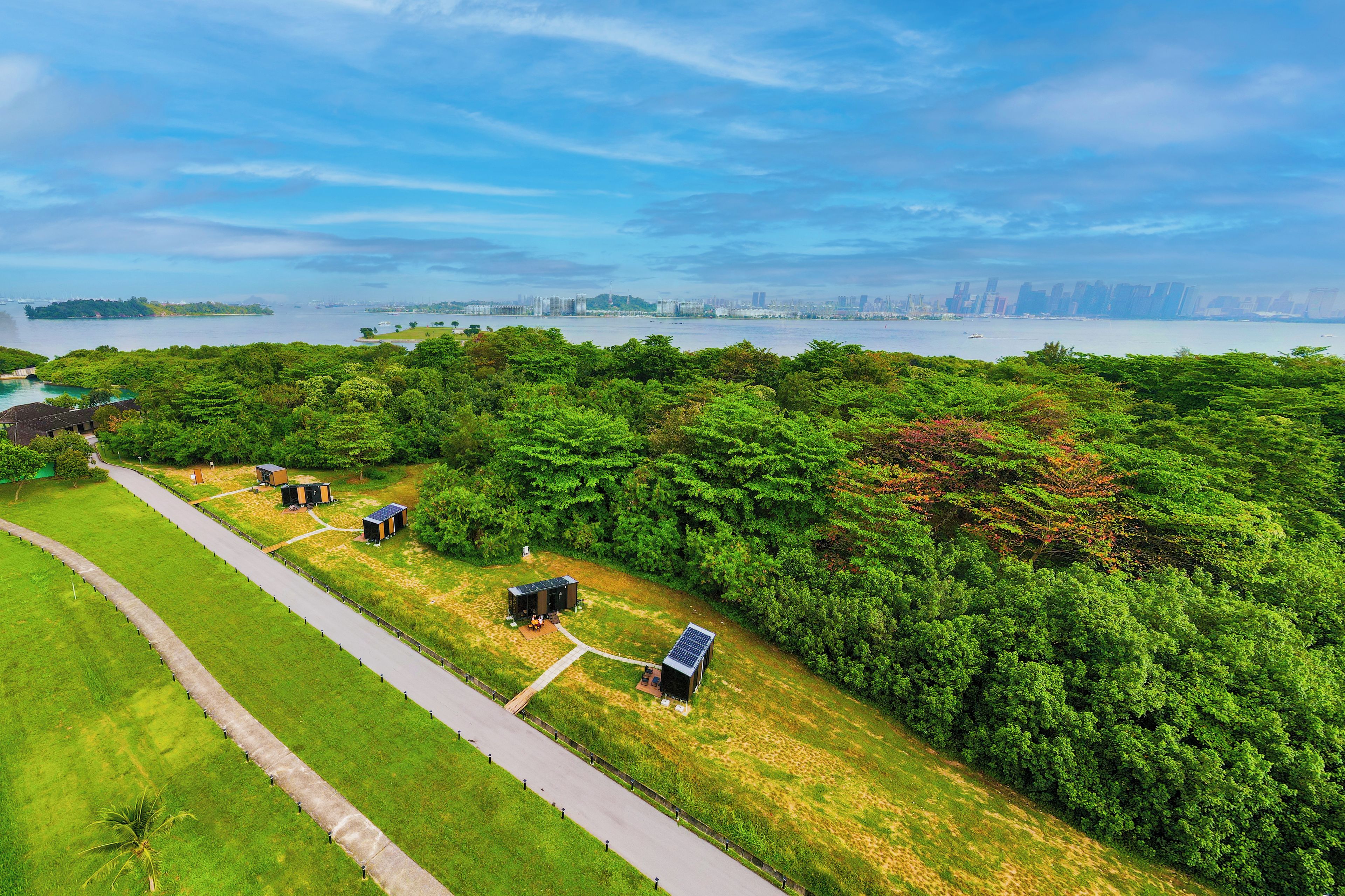A green park with a pathway, solar panels, and a city skyline in the distance.