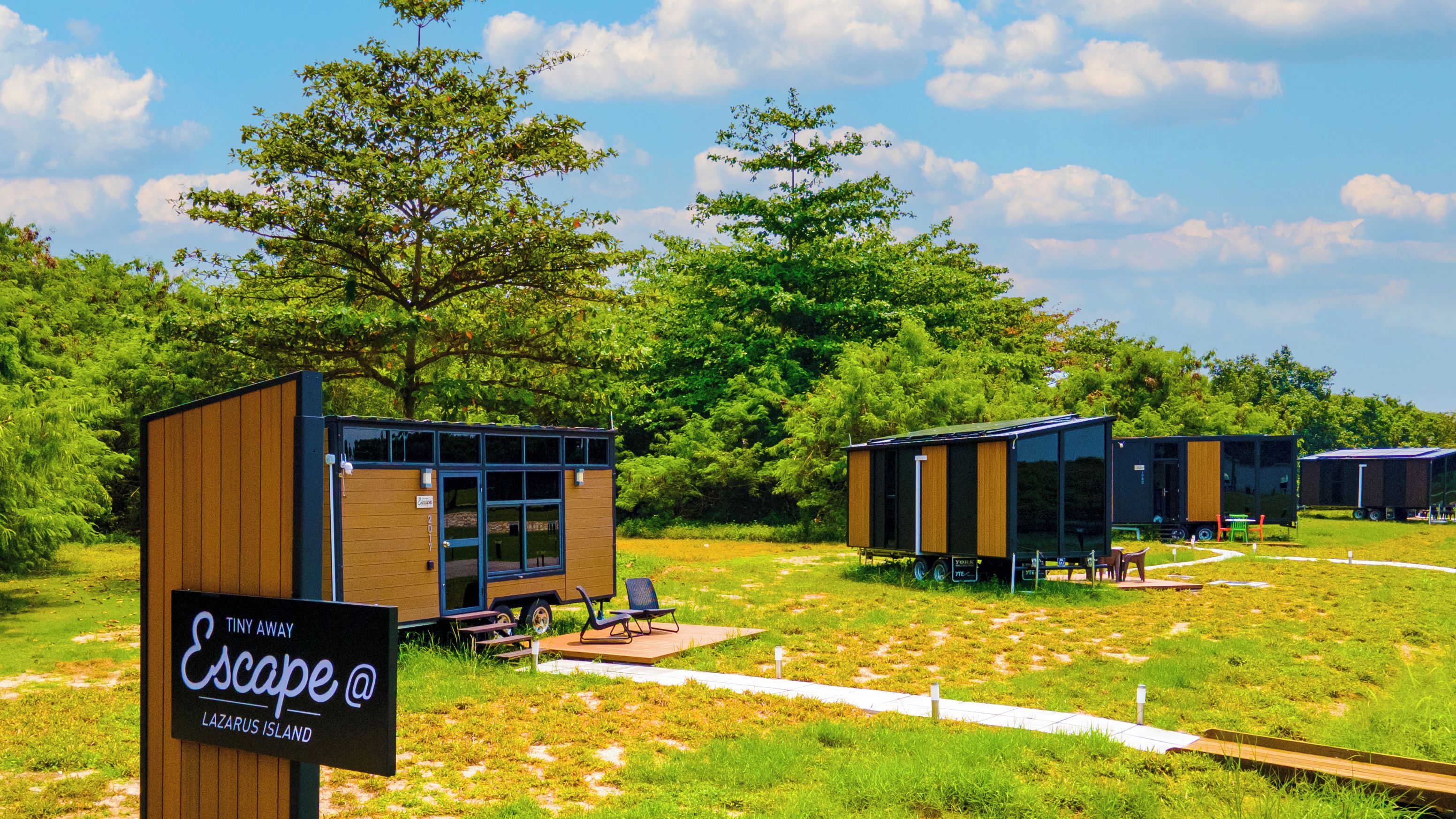 Een camping met moderne accommodaties, een picknicktafel en een bord met de tekst 'Escape @ Lazarus Island'.