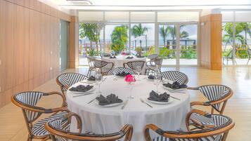 A dining area with round tables, wicker chairs, and a view of the ocean.