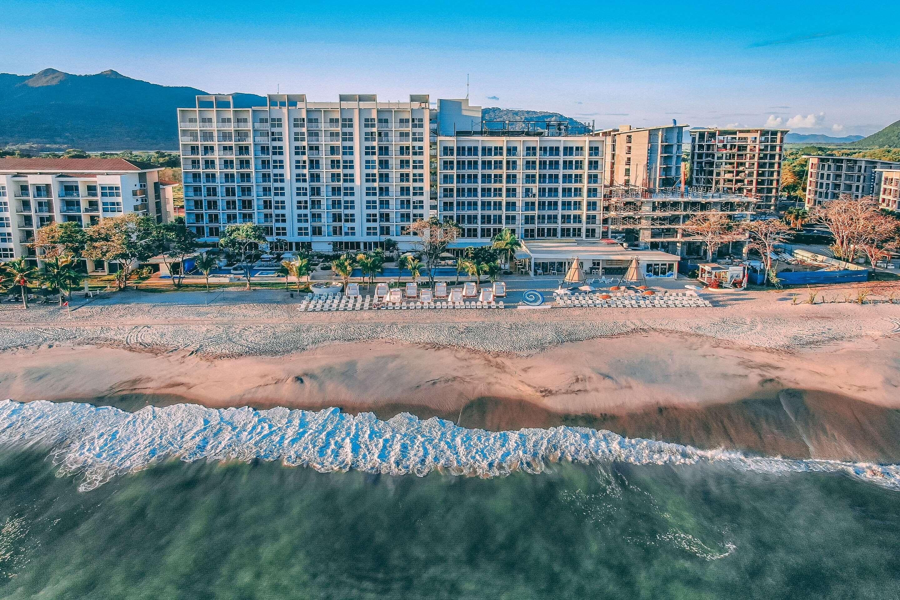A beachfront hotel with multiple buildings, a sandy beach, and a clear view of the ocean.